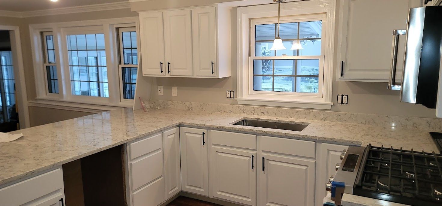 Bright white kitchen with granite countertops, white cabinets, windows, and stainless steel appliances