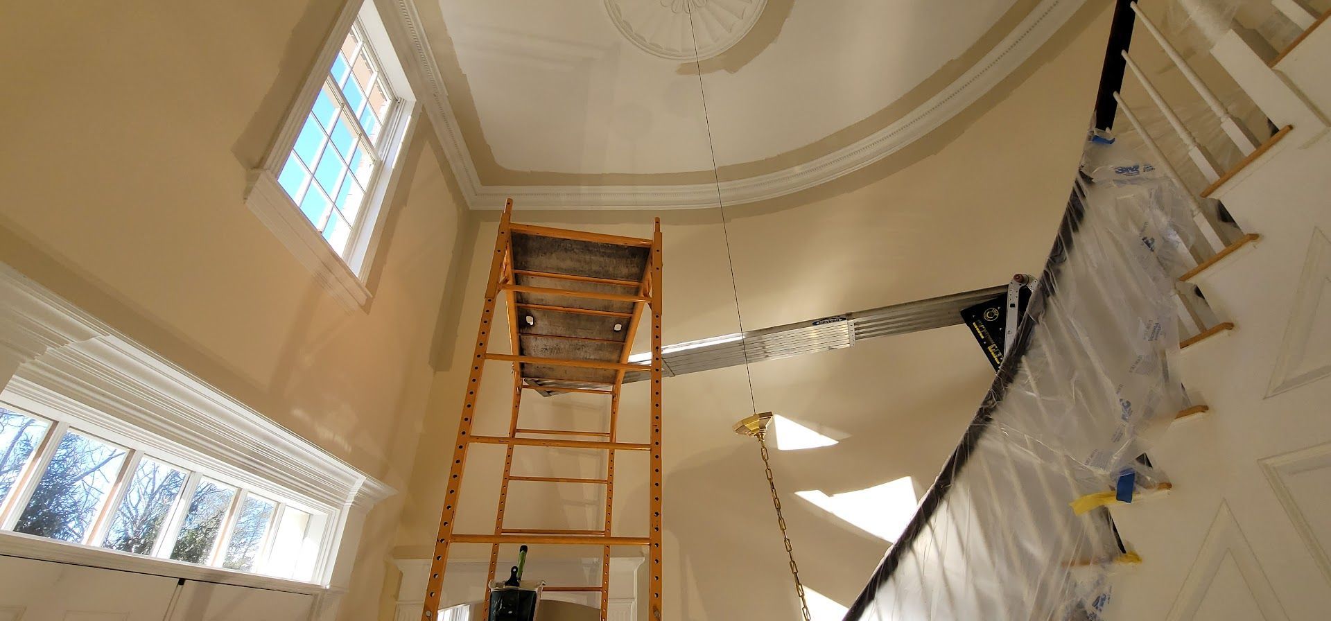 A tall room under renovation with scaffolding, ladders, and white walls under a domed ceiling.