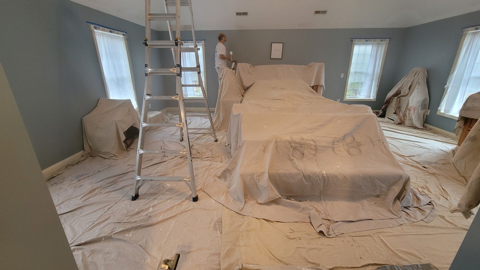 A room covered in plastic sheeting with a ladder in the center, likely being painted or renovated.