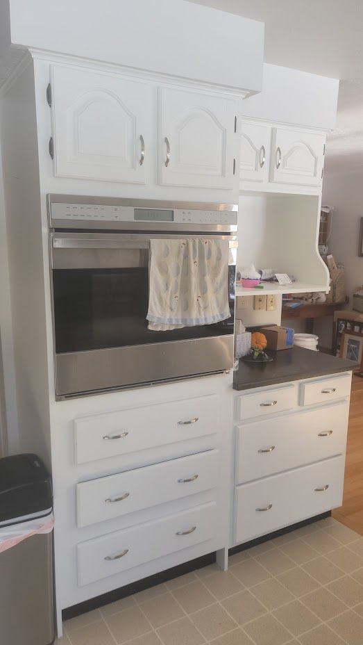 White built-in kitchen cabinet with oven, drawers, and shelves in a tiled room