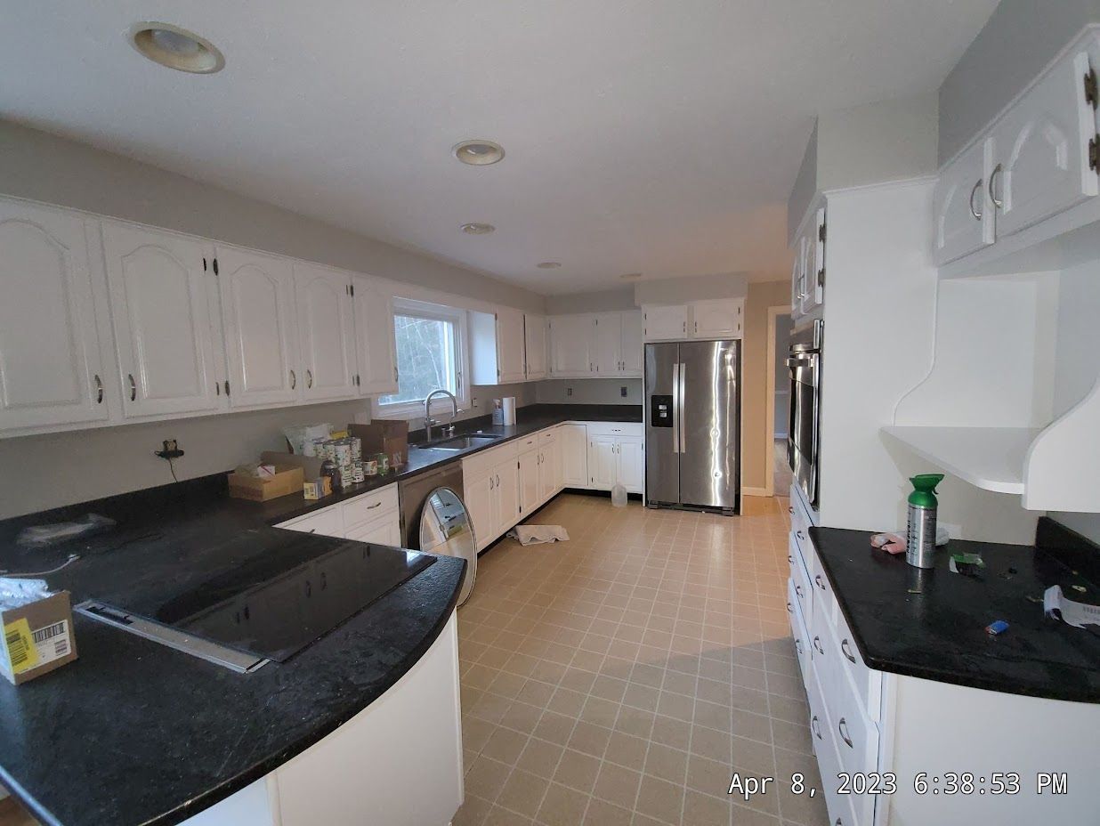 Bright kitchen with white cabinets, black countertops, tan tile floor, and stainless steel refrigerator