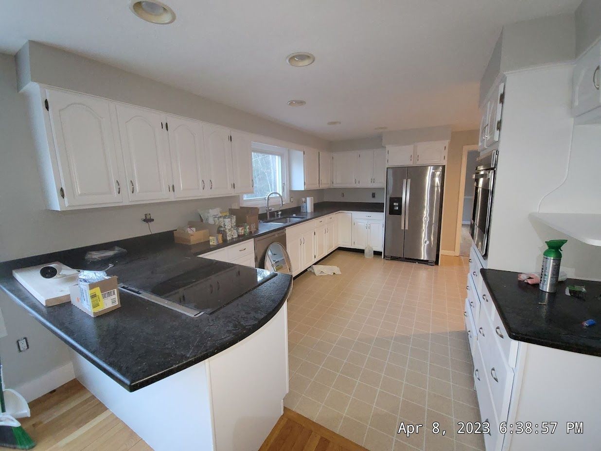 Bright kitchen with white cabinets, black countertops, tile floor, and stainless steel refrigerator.