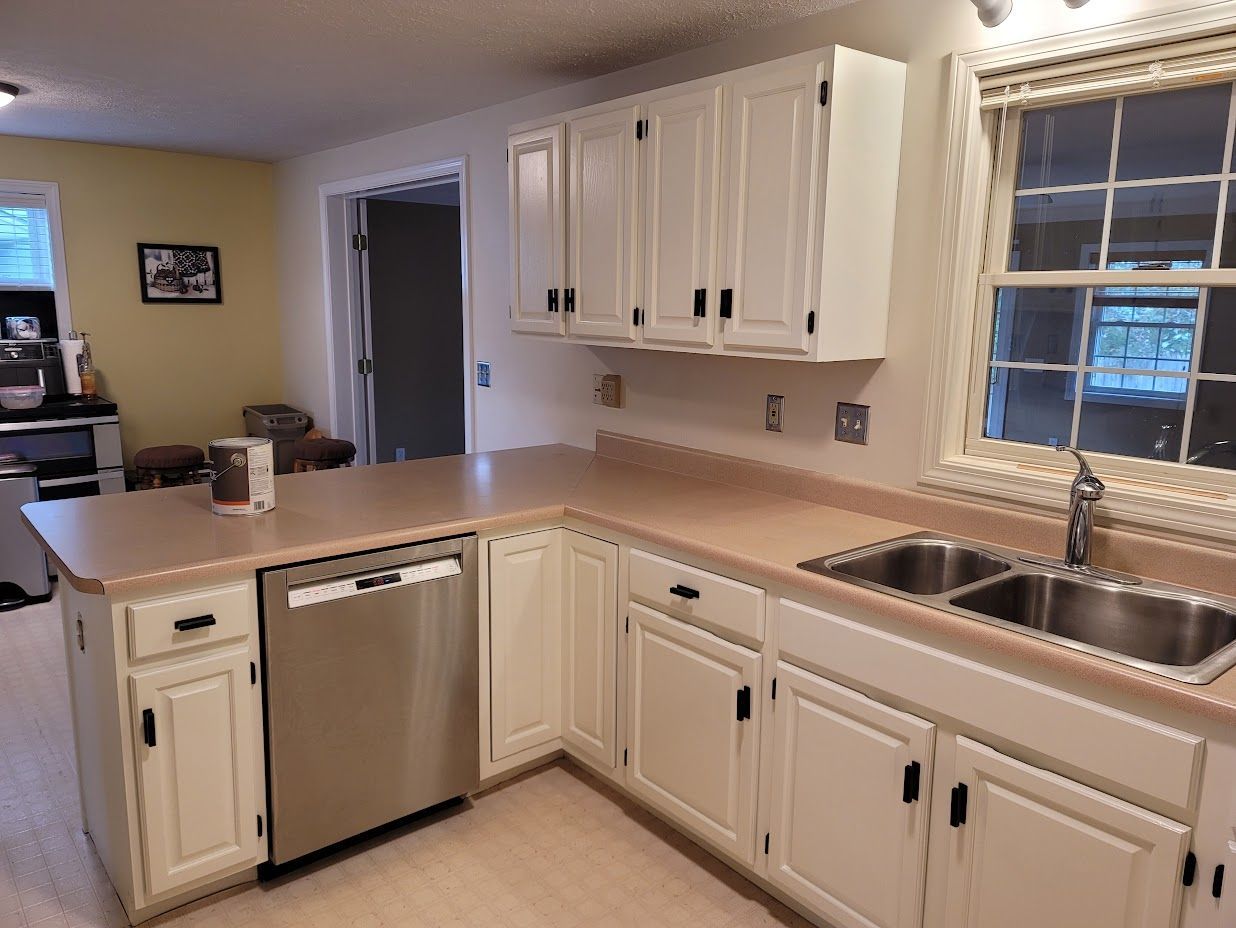 Bright white kitchen with wood countertops, stainless dishwasher, double sink, and a window above the counter
