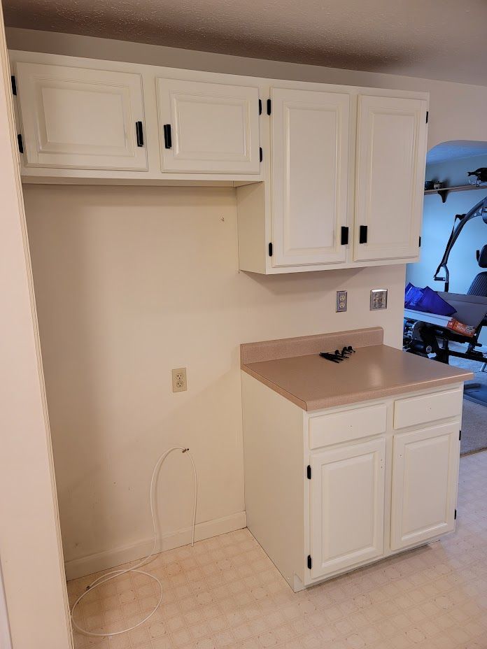 White kitchen cabinets and beige countertop in a small, empty kitchenette area.