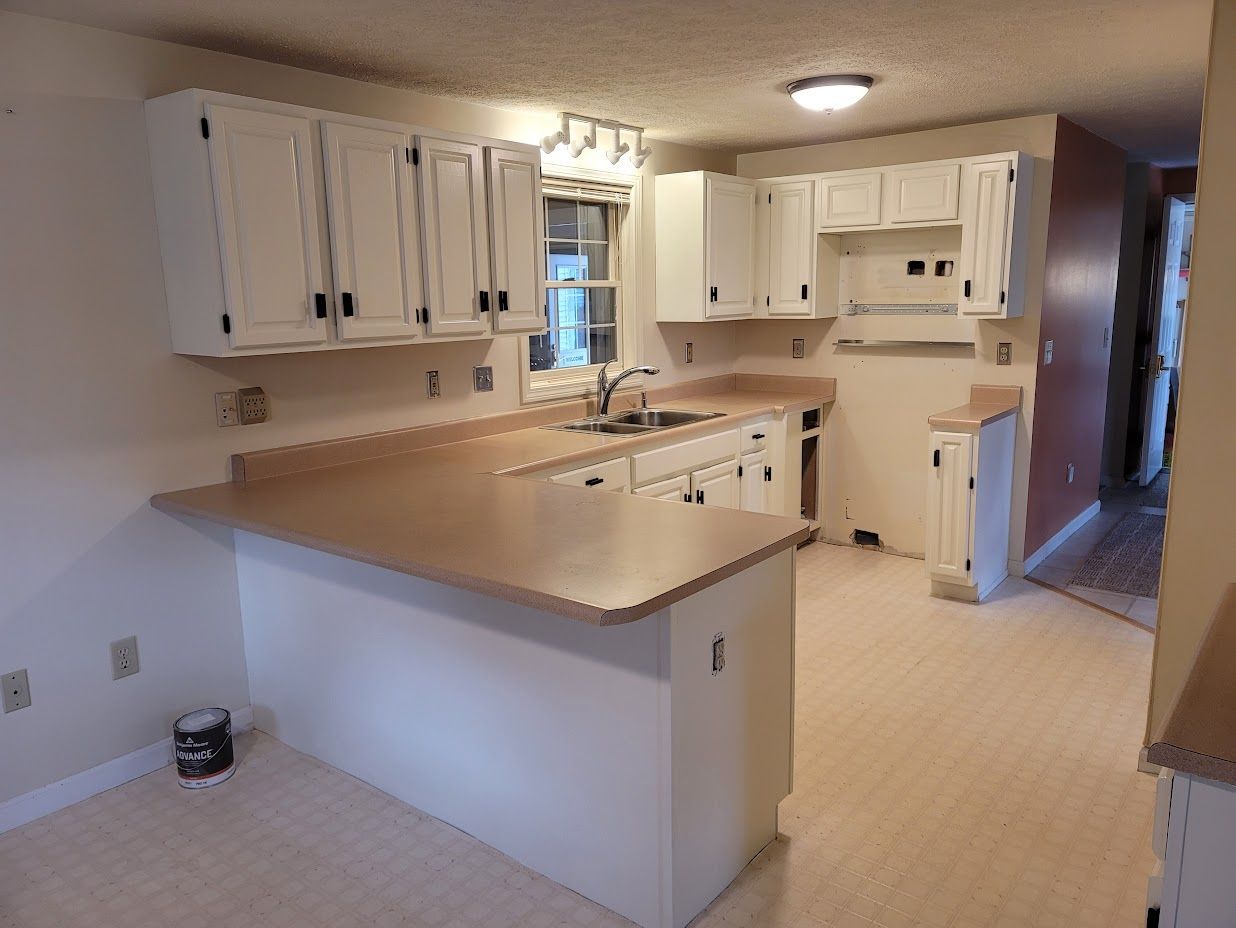 Empty kitchen with white cabinets, tan countertops, and a central island under ceiling lights.