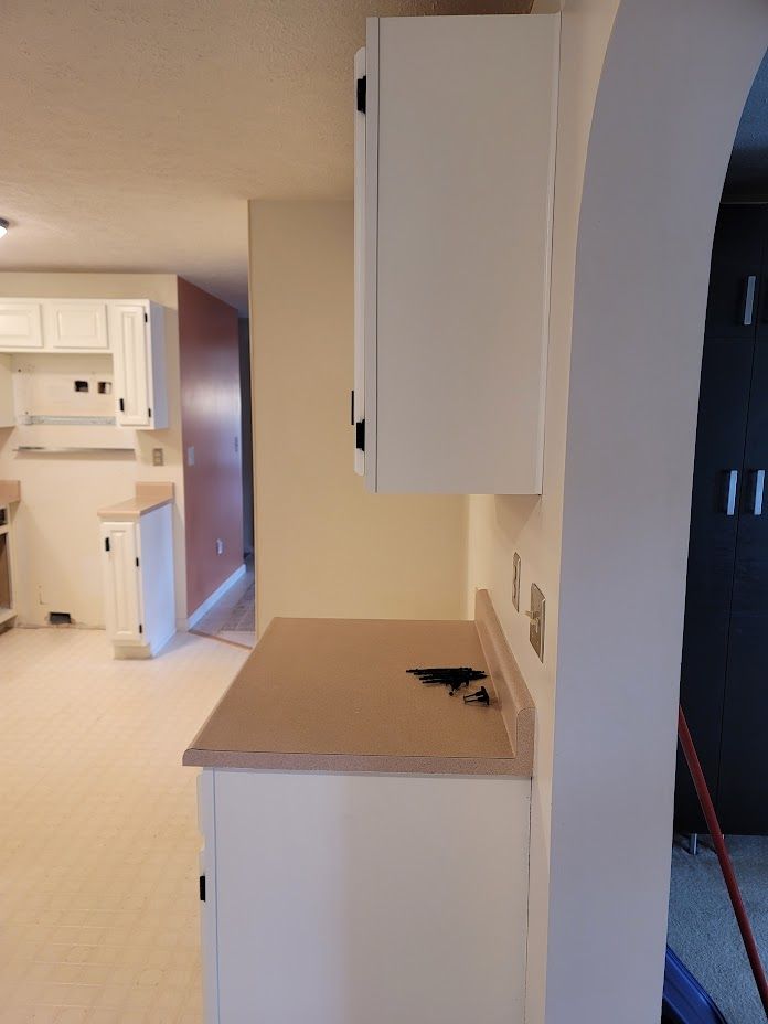 Hallway with white cabinets, beige countertop, and an arched doorway leading to a kitchen.