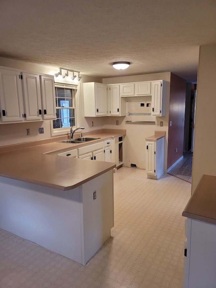 Empty cream-colored kitchen with white cabinets, peninsula counter, and overhead light.