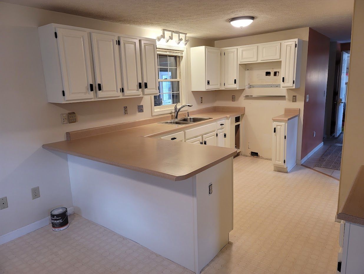 Empty white kitchen with beige counters, cabinets, and tiled floor, viewed from the dining area