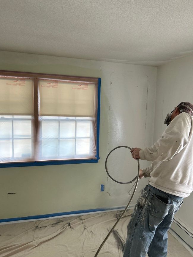 Person standing in an unfinished room, holding a coiled cable near a window being painted or repaired