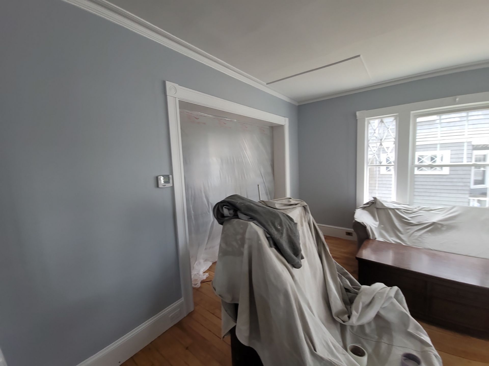 Gray bedroom under renovation with furniture covered in drop cloths and a doorway to another room