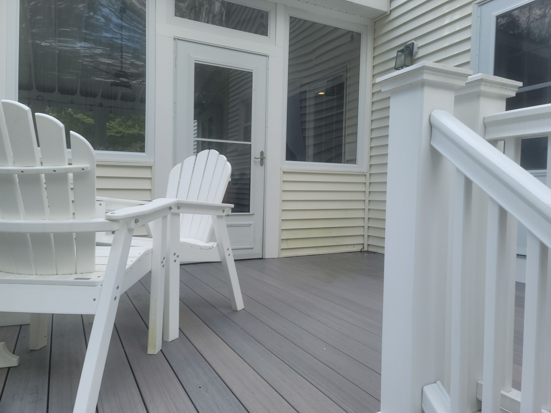 White patio chairs on a gray deck beside a beige house and sliding glass door