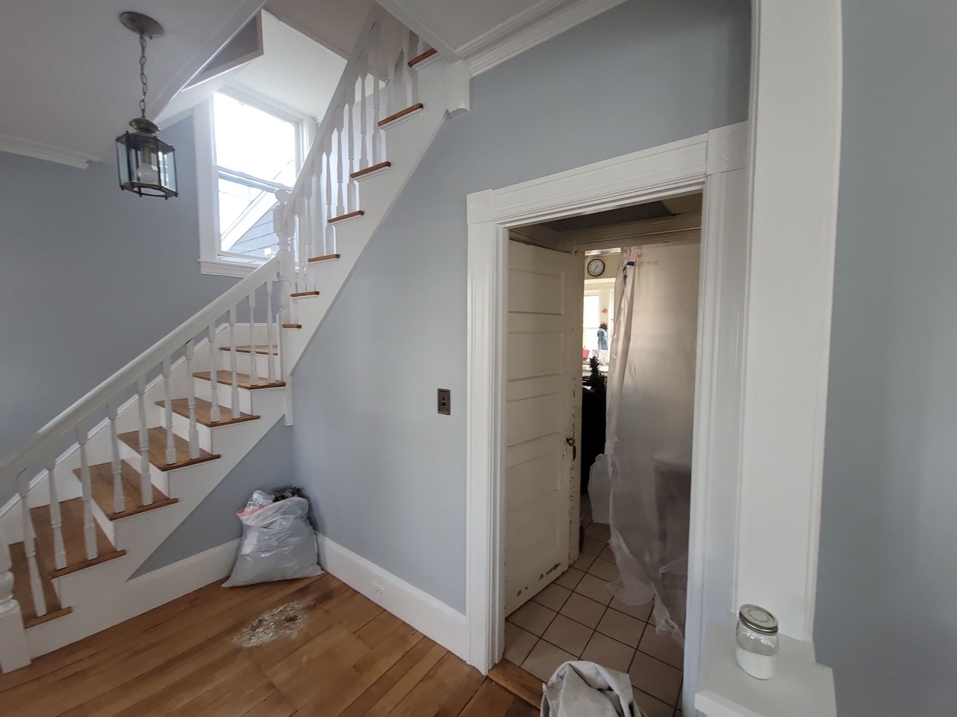 Staircase in a light gray hallway beside a doorway and tiled room, with hardwood floor and hanging lanterns.