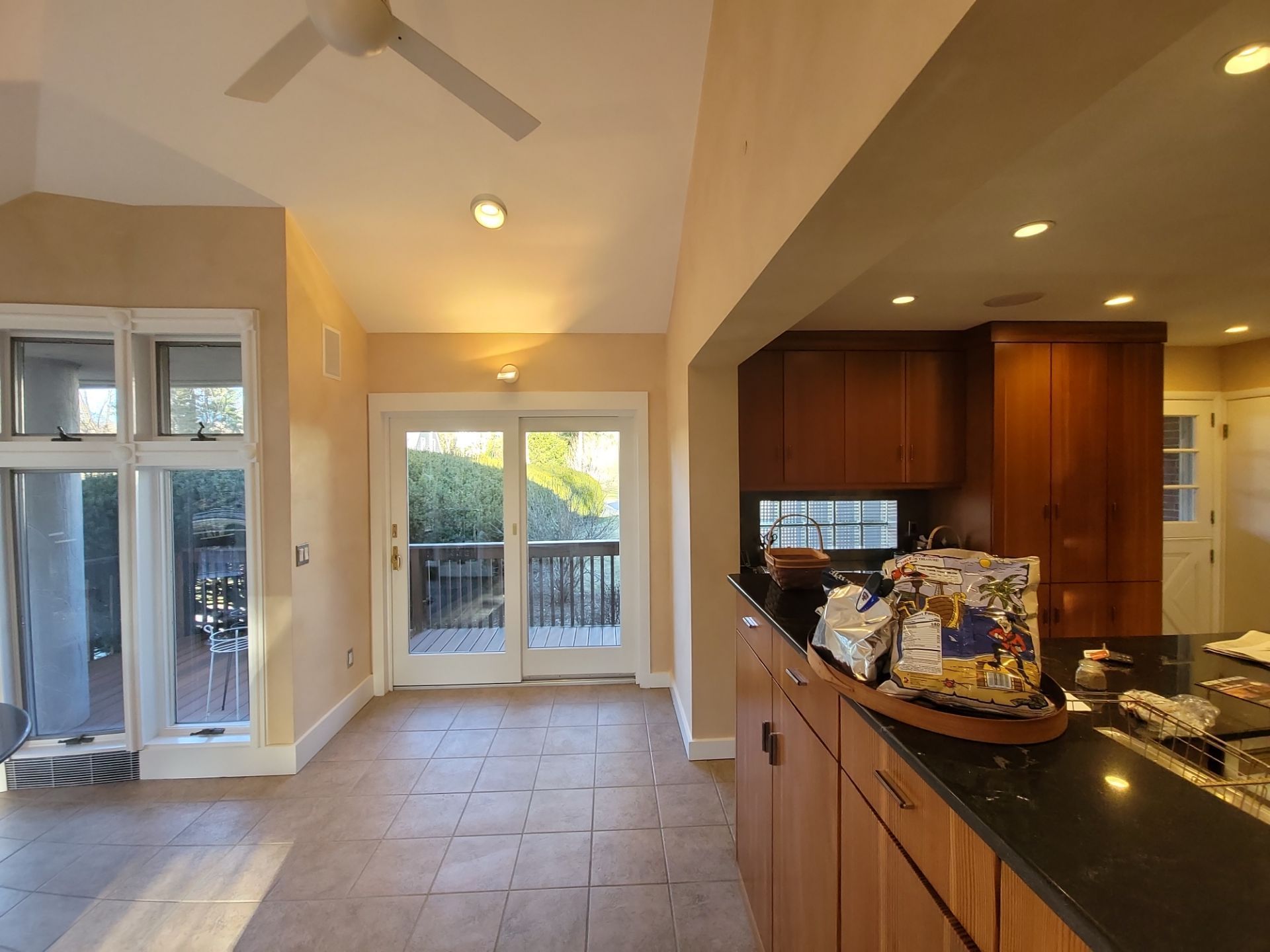 Open kitchen with black countertop, wood cabinets, tile floor, and bright glass doors leading outside