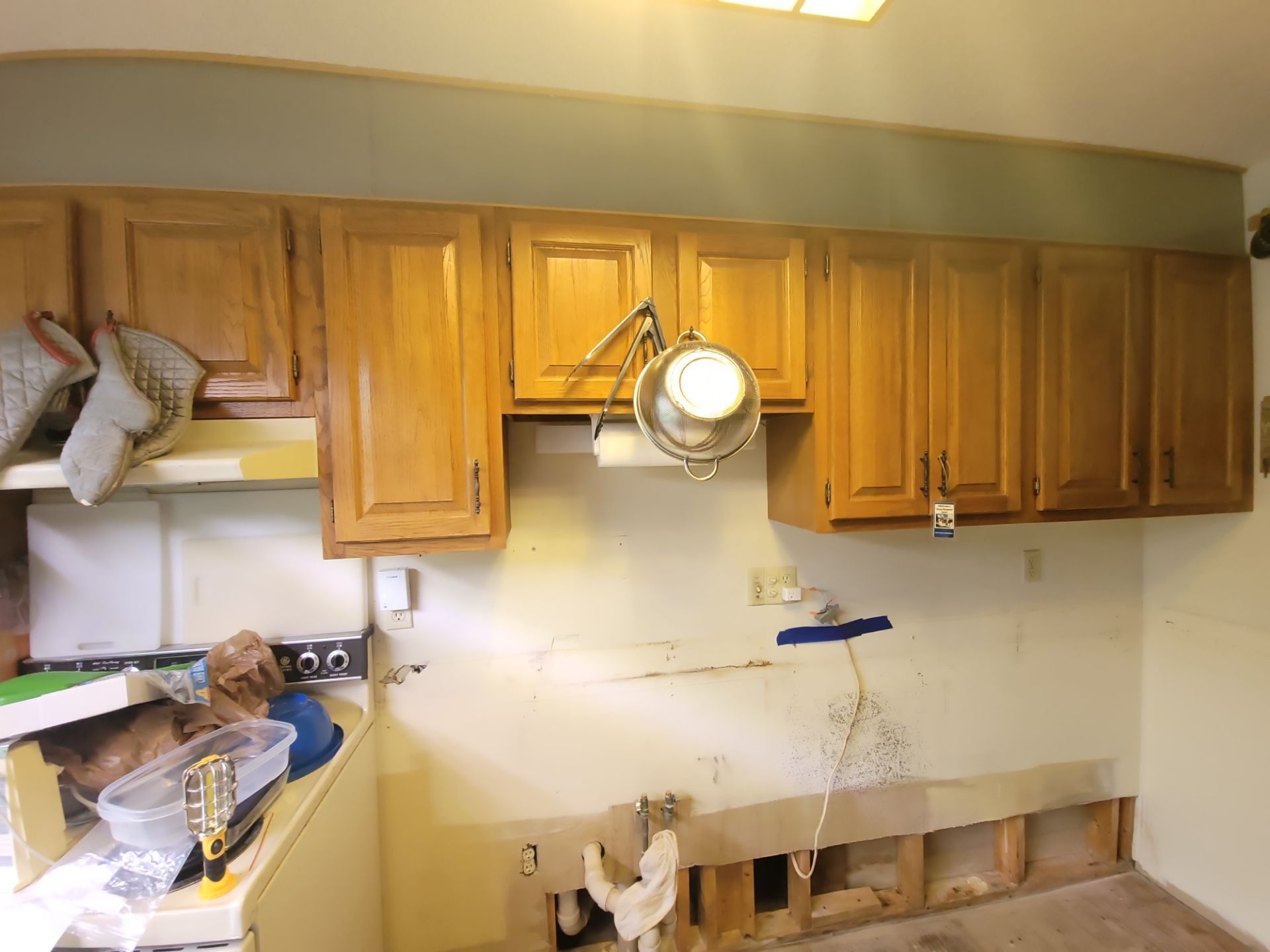 Kitchen under renovation with removed lower cabinets, exposed wall, and wood upper cabinets.