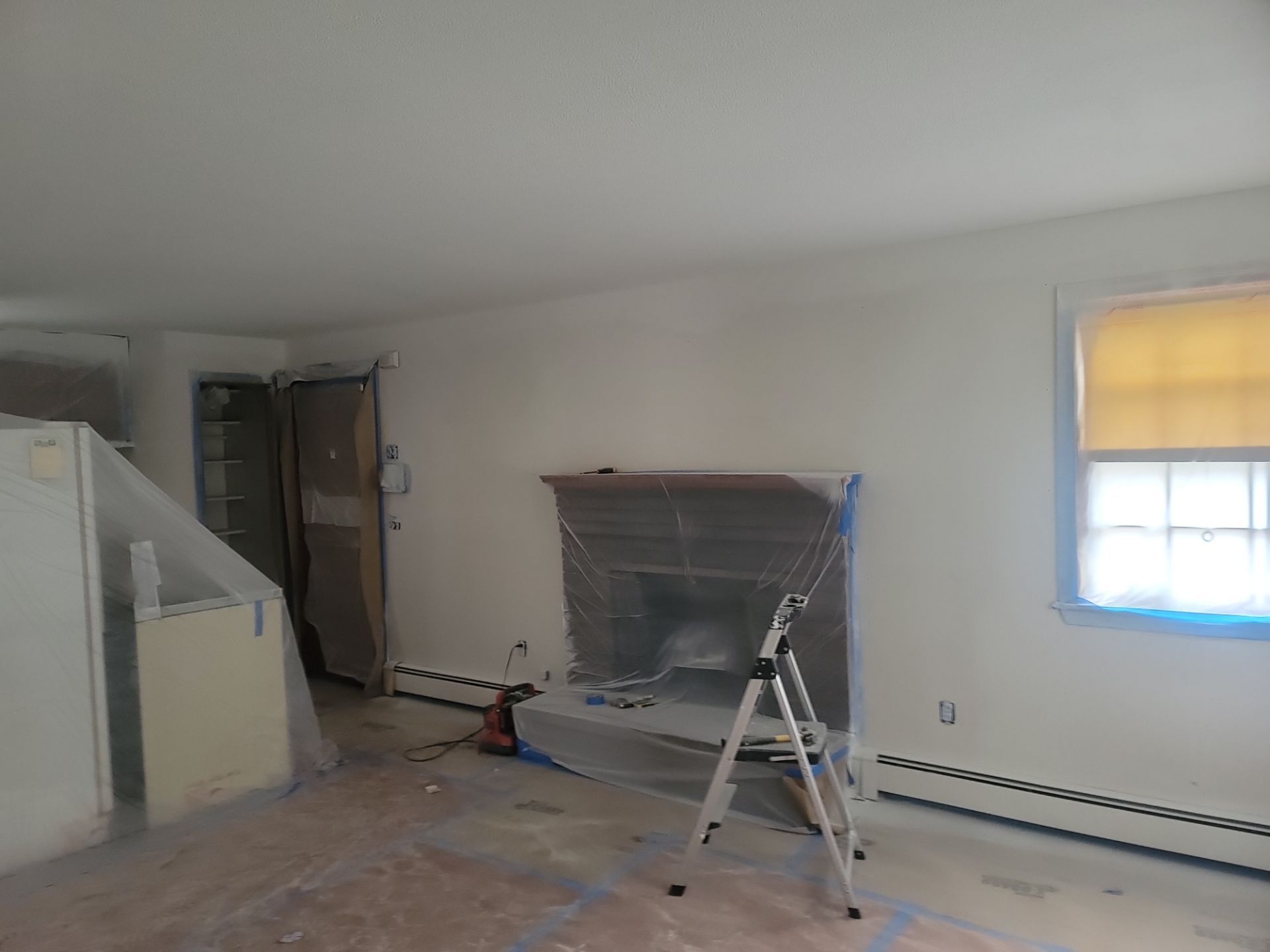 Empty living room with ladder, fireplace, staircase, and window shade during renovation