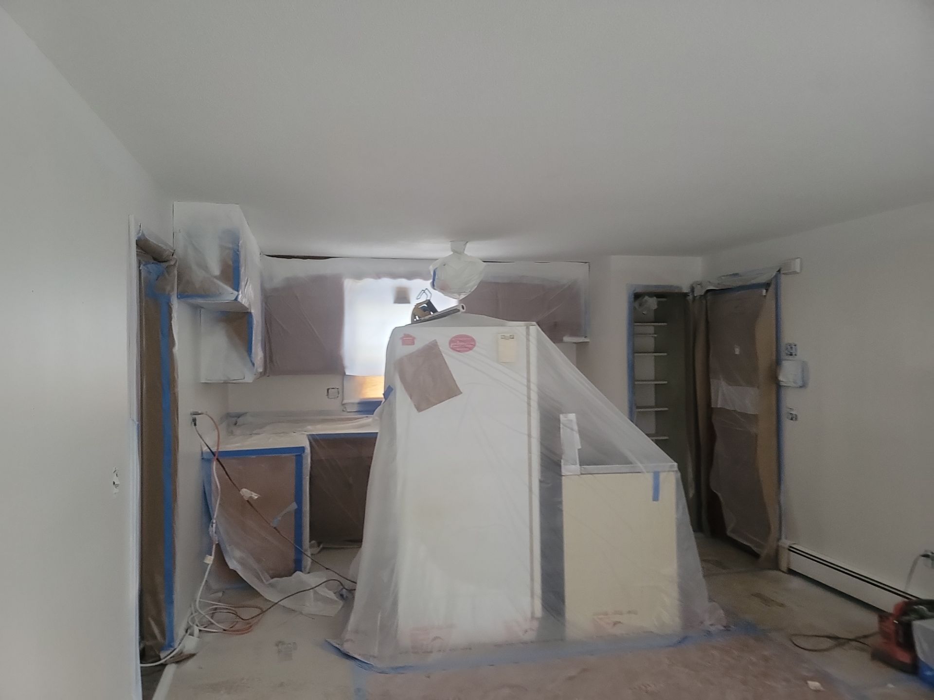 Dust-covered room under renovation with covered furniture, exposed walls, and debris on the floor