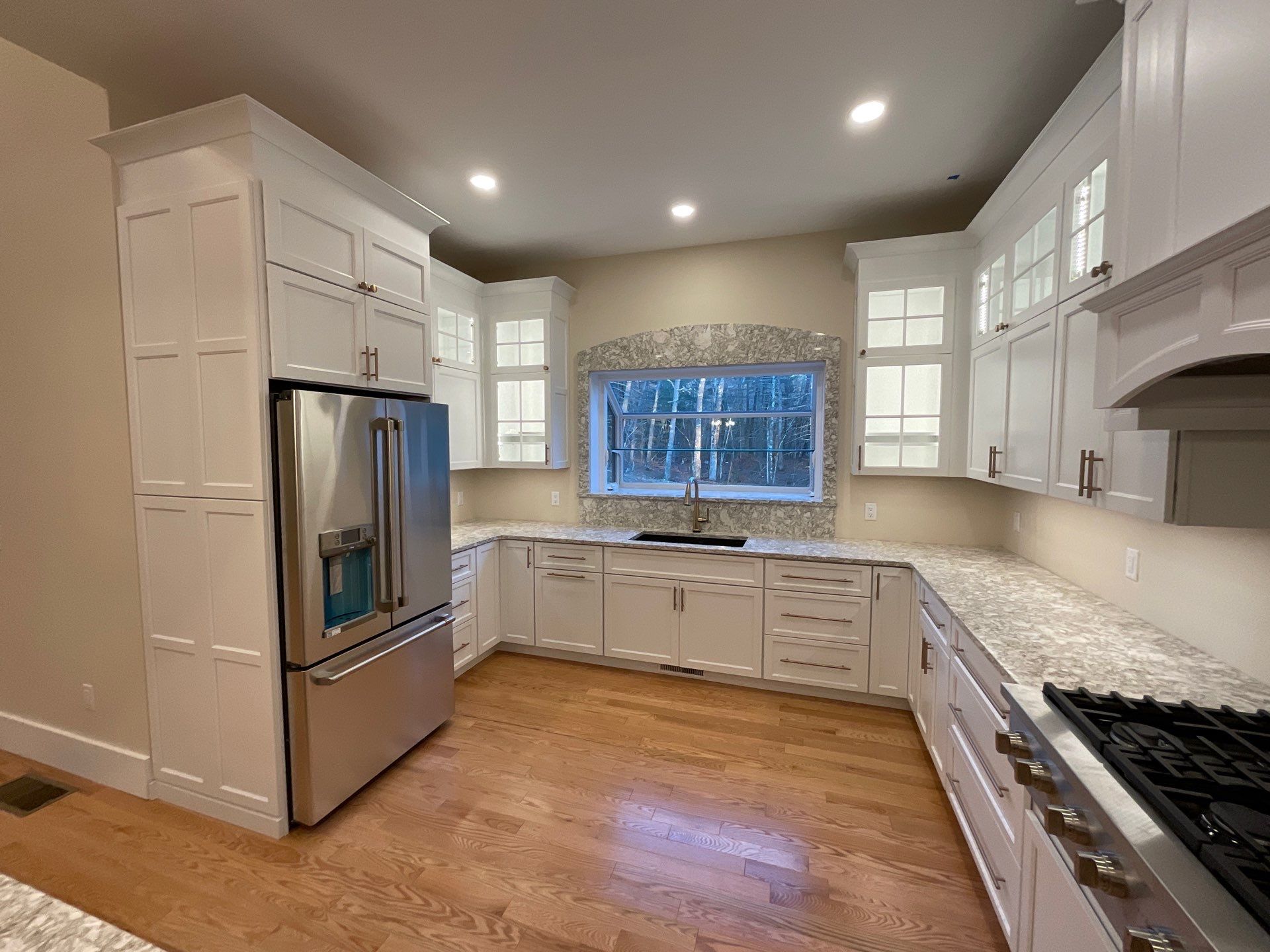 Bright kitchen with white cabinets, stainless steel refrigerator, gas stove, and hardwood floors