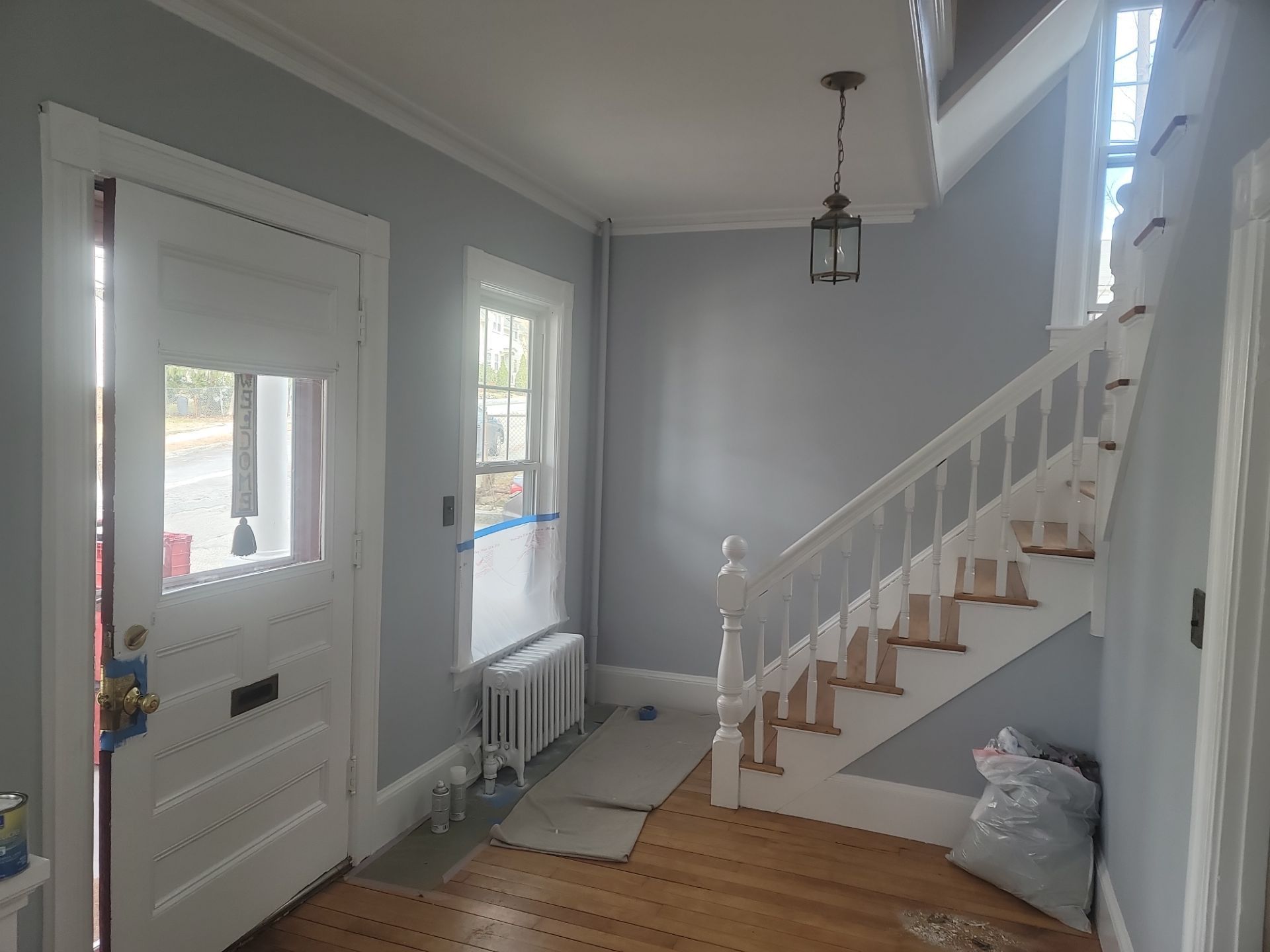 Small entryway with white front door, staircase, window, radiator, and light wood floor.