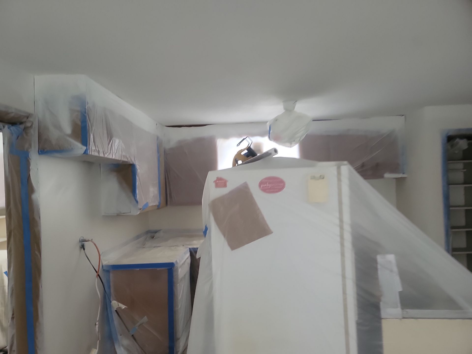 Plastic-covered room with taped furniture, boxes, and a ladder, suggesting renovation or painting in progress