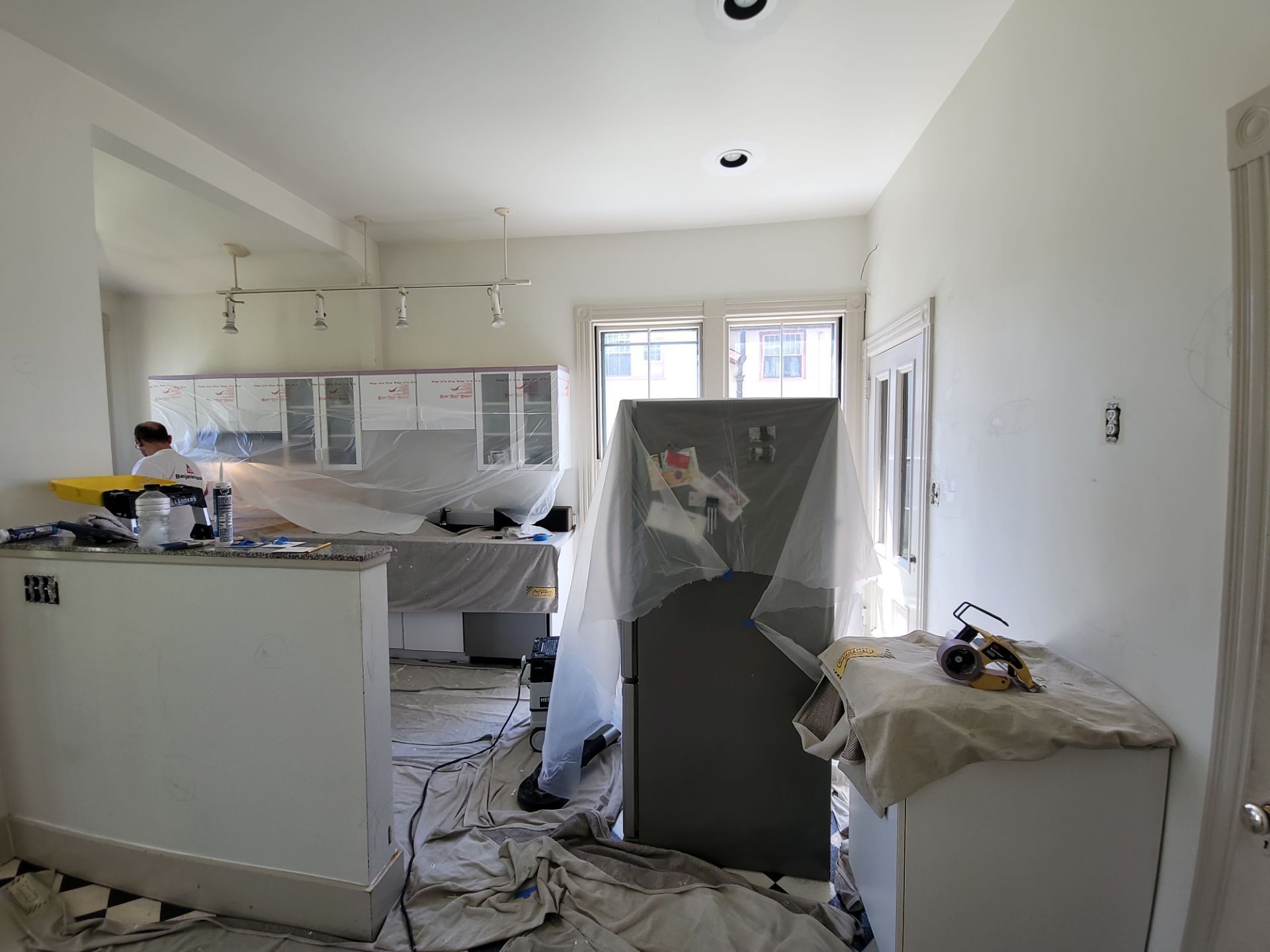 Partially renovated kitchen with cabinets, appliances, and covered items amid construction debris