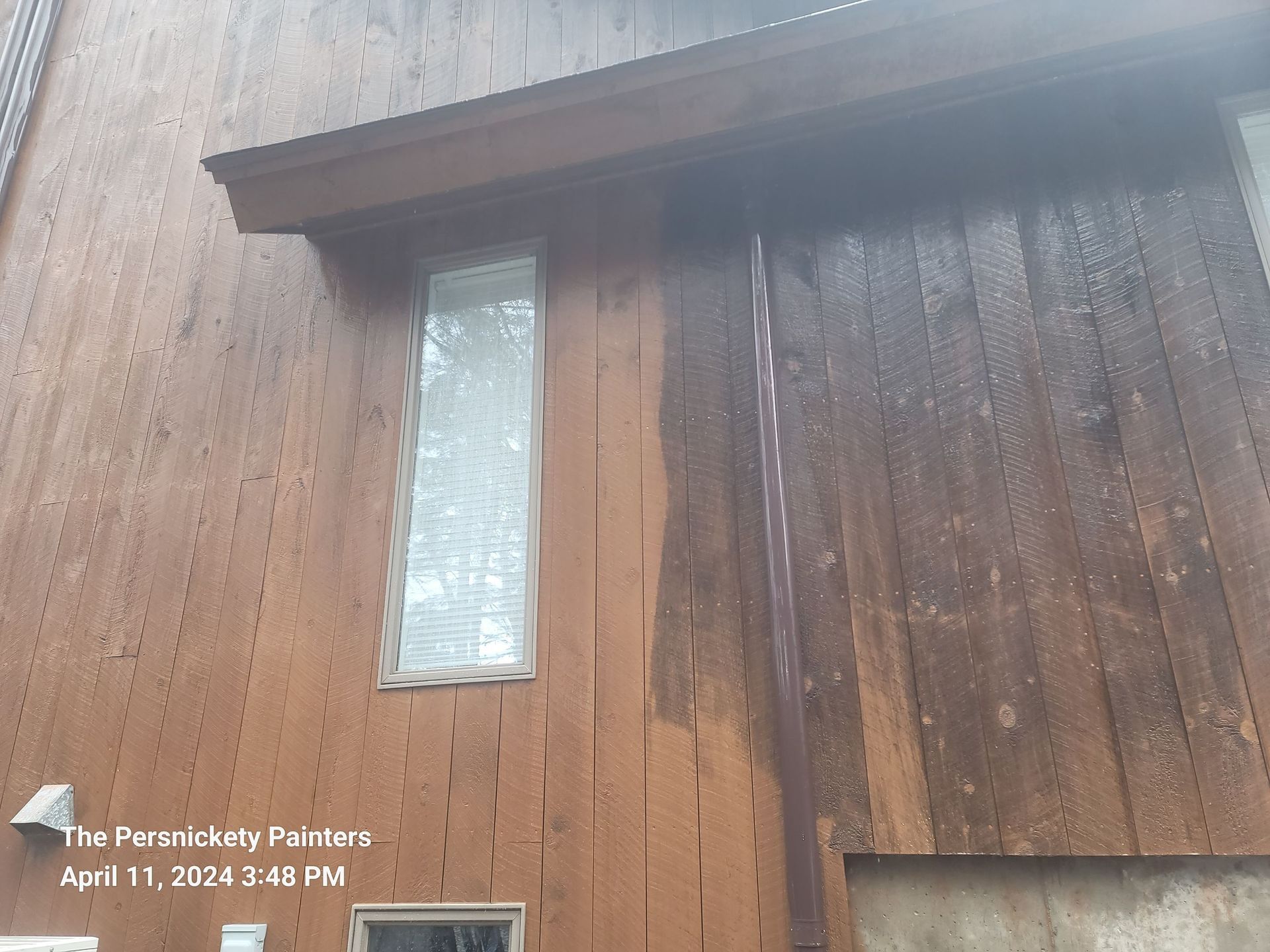 Wooden exterior wall with a narrow frosted window and a door under a roof overhang.