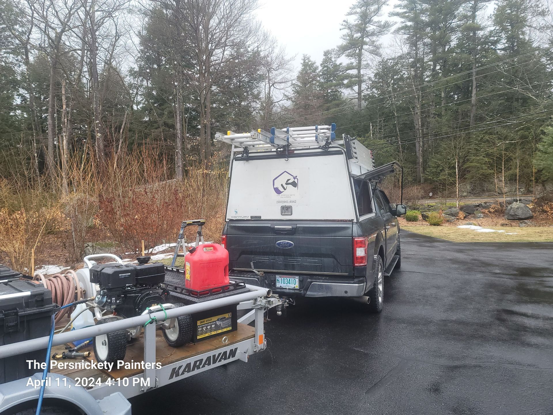 Van parked on a wet road beside a utility trailer and gear in a wooded area