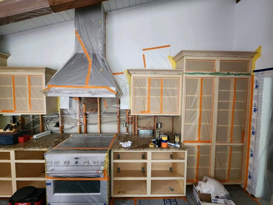 Kitchen under renovation with plastic-covered cabinets, taped appliances, and a large mesh-covered pantry cabinet