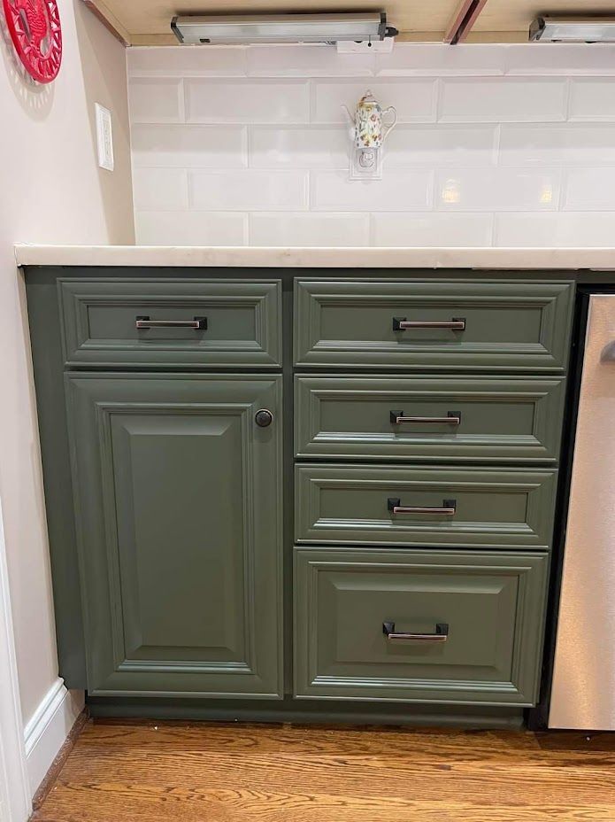 Green kitchen cabinet with drawers and a door beneath a countertop, shown against a white tiled wall.