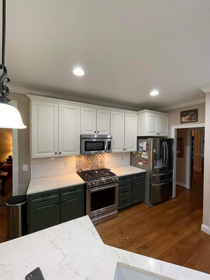 Modern kitchen with white cabinets, stainless steel appliances, dark lower cabinets, and wood floors.