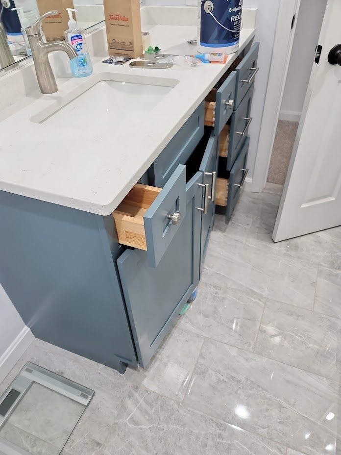 Bathroom vanity with open drawers, a white countertop, and a sink on light gray tile flooring.