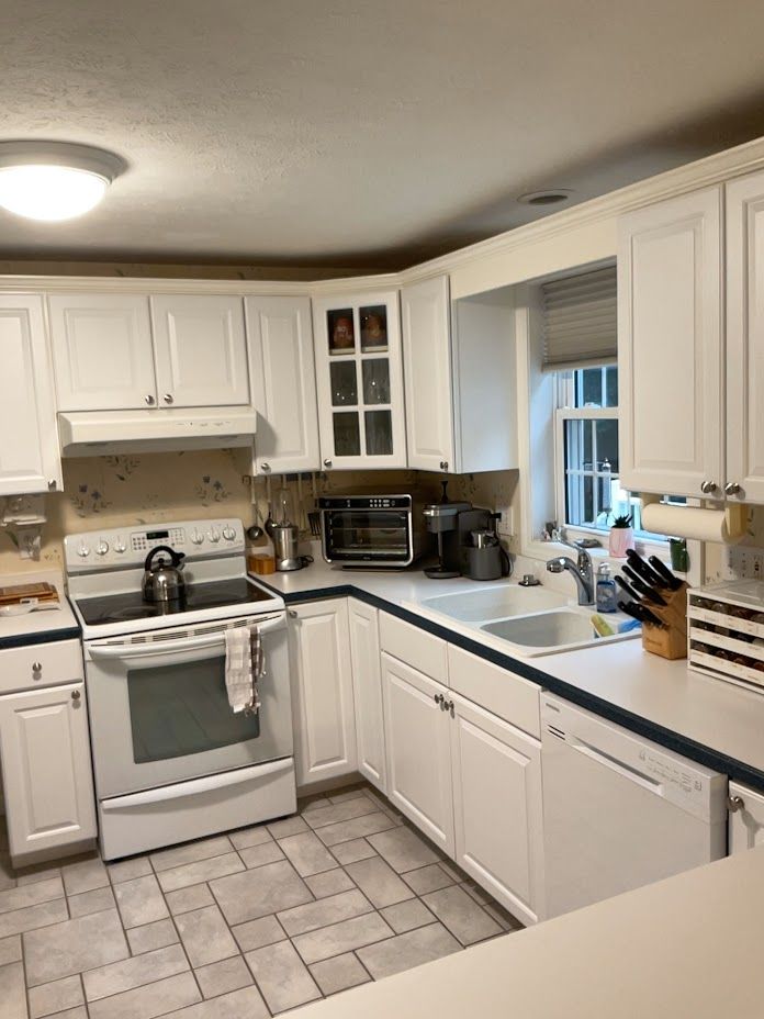 Bright white kitchen with stove, sink, cabinets, tiled floor, and a window over the counter.