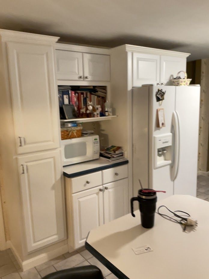 White kitchen with cabinets, refrigerator, microwave, and a table holding a black tumbler and glasses.
