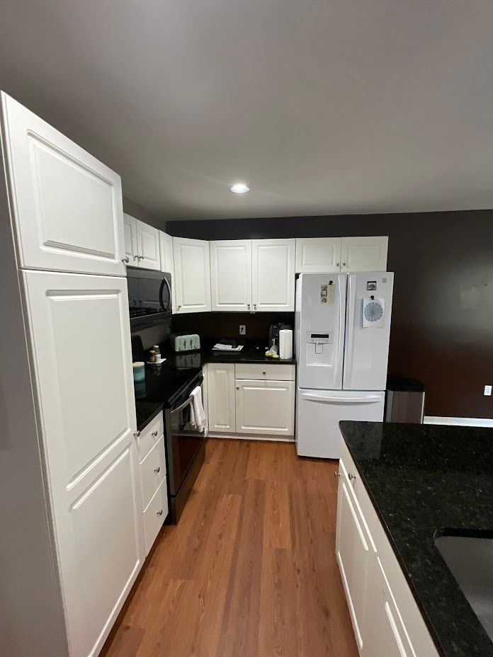 Modern kitchen with white cabinets, black countertops, stainless appliances, and wood flooring