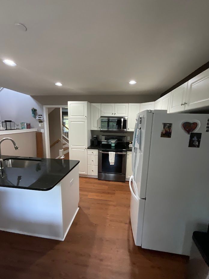 Modern kitchen with white appliances, black island countertop, wood floors, and recessed ceiling lights