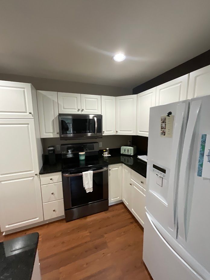 White kitchen with black appliances, hardwood floor, and white cabinets, viewed from a corner.