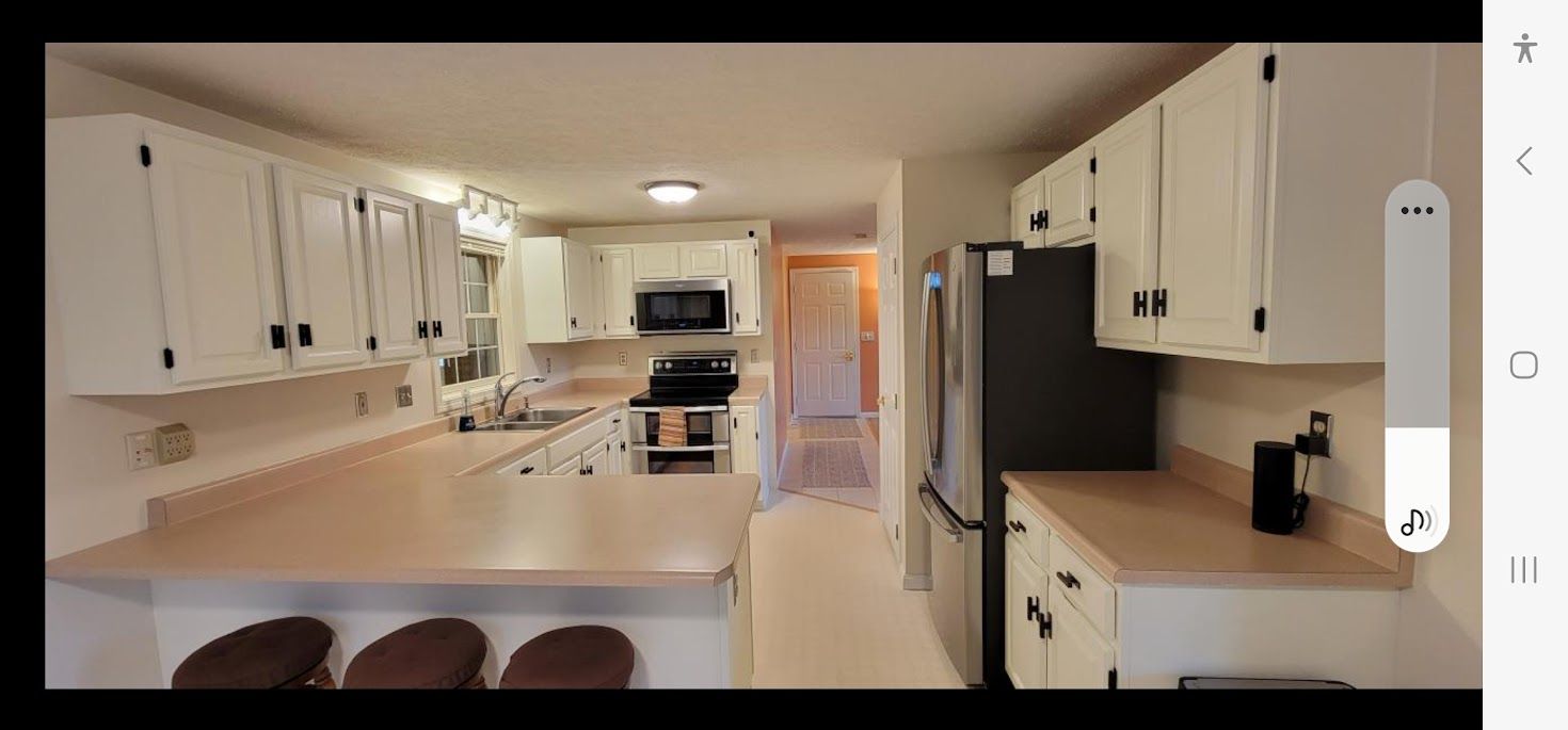 Bright white kitchen with island, stainless fridge, stove, and tan countertops in a well-lit home interior