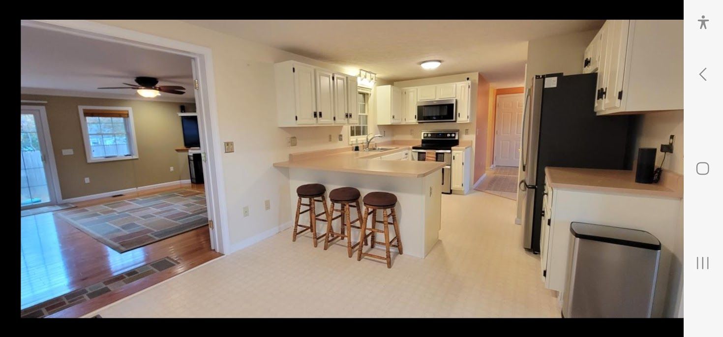 Bright kitchen with white cabinets, island stools, and a view into a living room with hardwood floors