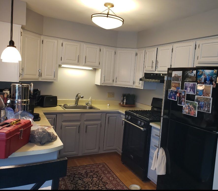 Small kitchen with white and gray cabinets, black appliances, and a refrigerator covered in photos.