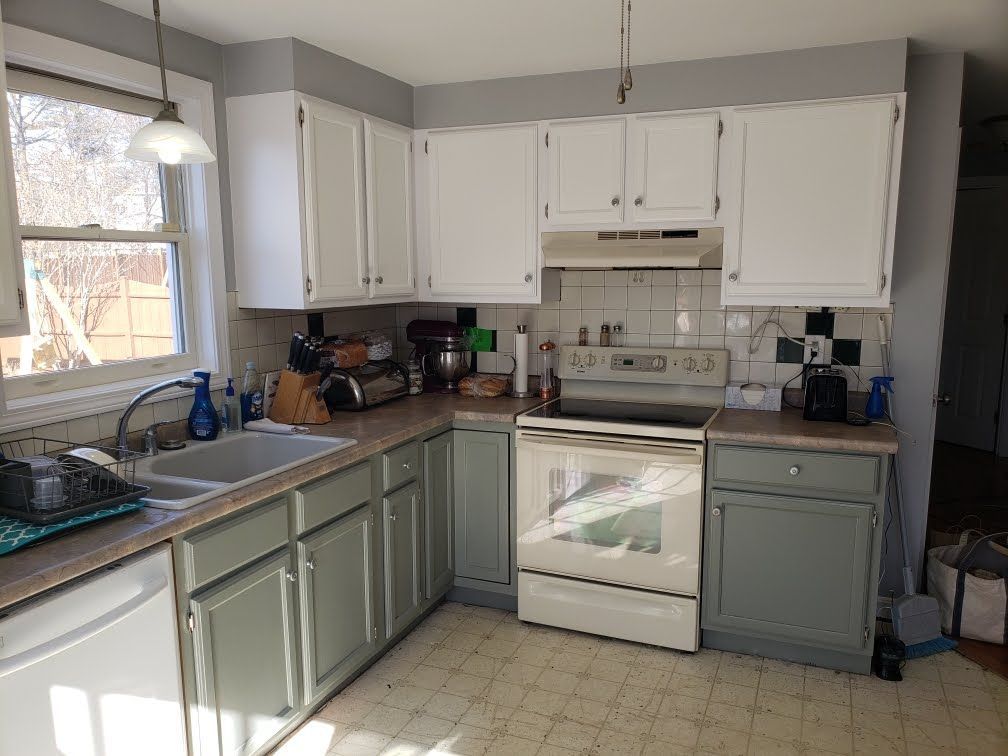 Small kitchen with white cabinets, gray lower cabinets, stove, sink, and counter appliances.