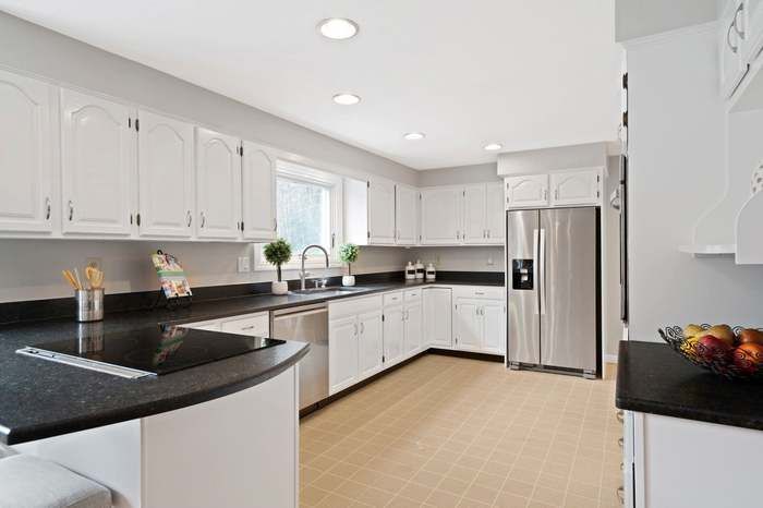 Bright modern kitchen with white cabinets, black countertops, stainless steel fridge, and light wood flooring