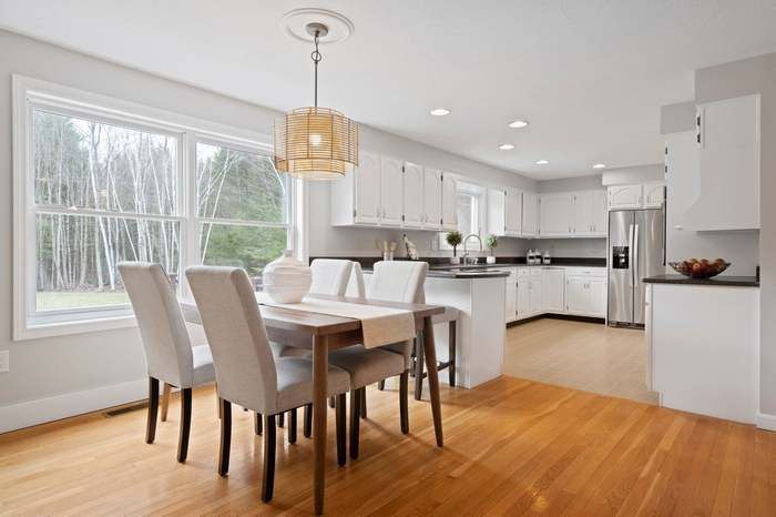 Bright open dining room with white chairs, hardwood floors, and a modern kitchen in the background