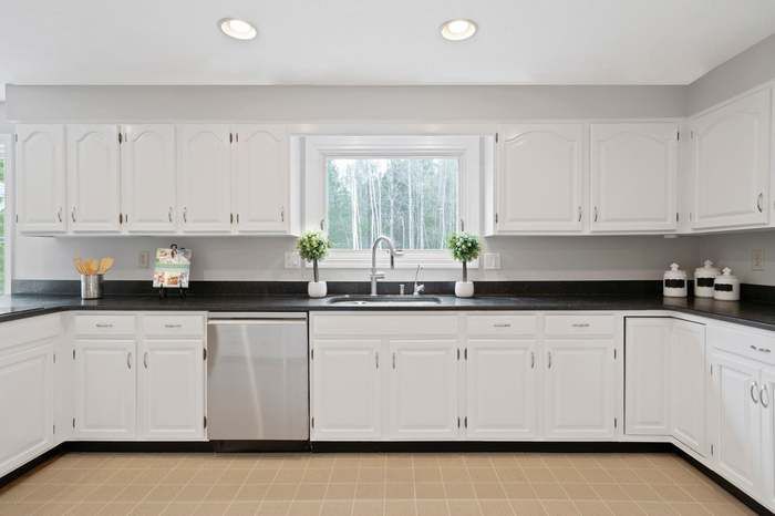 Bright white kitchen with black countertops, stainless dishwasher, and window above the sink.