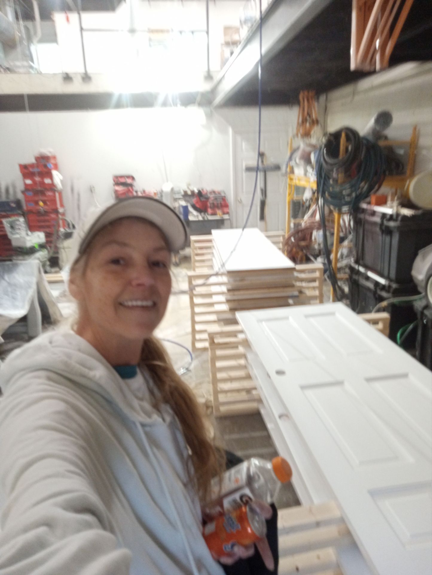 Person smiling in a workshop beside stacked white cabinet doors and tools