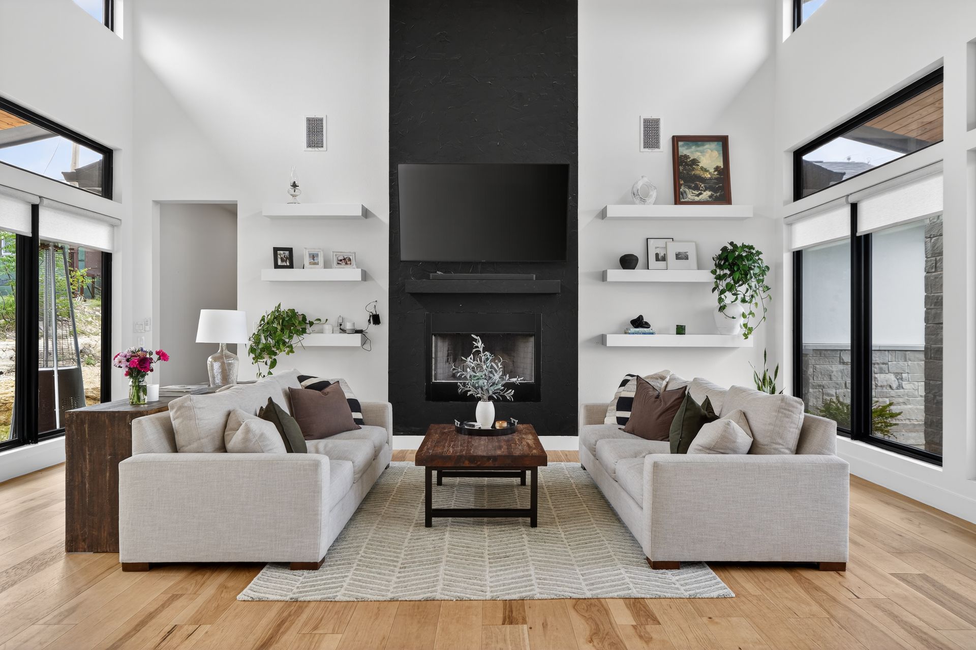 Bright modern living room with two gray sofas, a black fireplace, and large windows overlooking the outdoors