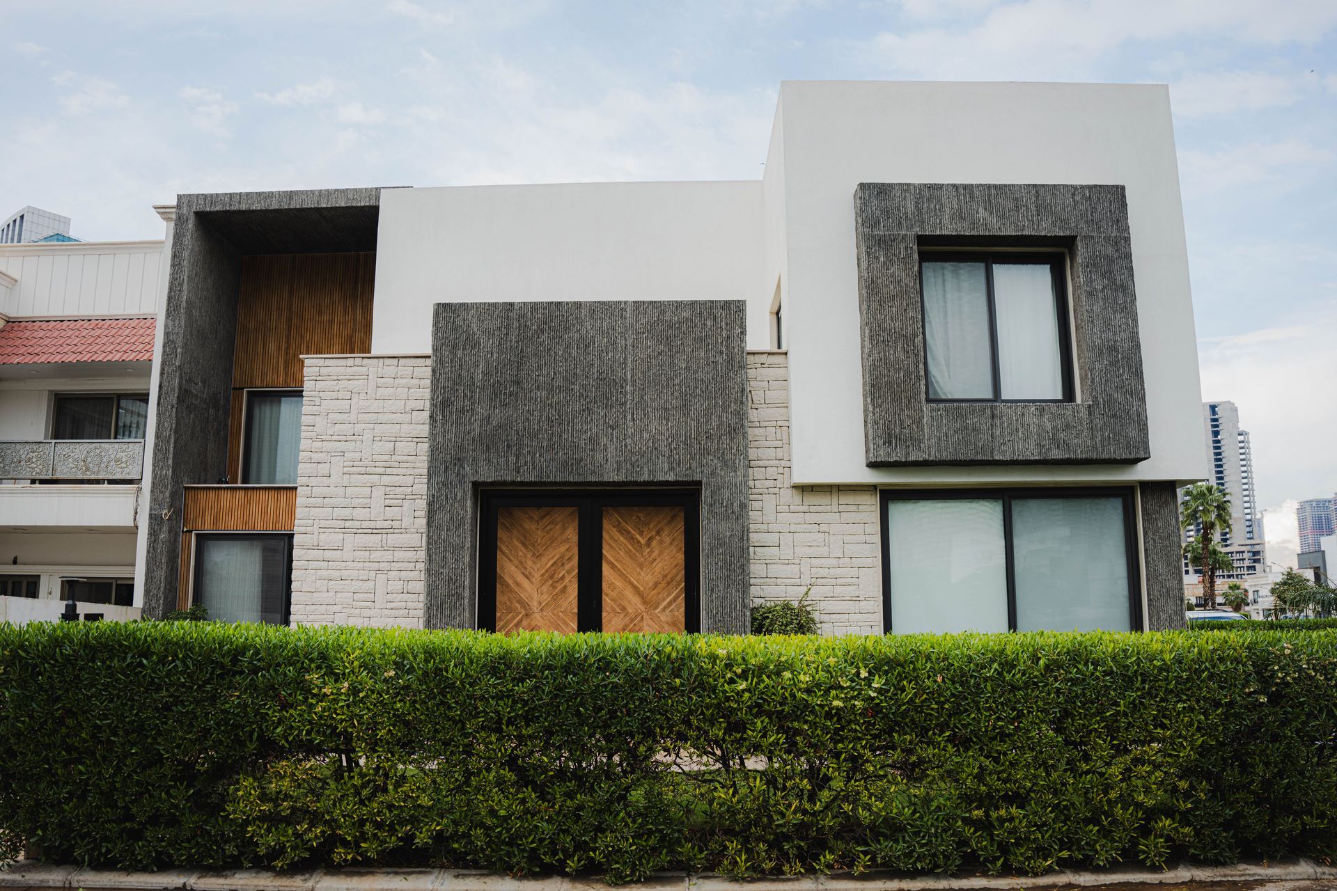 Modern two-story house with white and gray facade, large windows, and a hedge in front