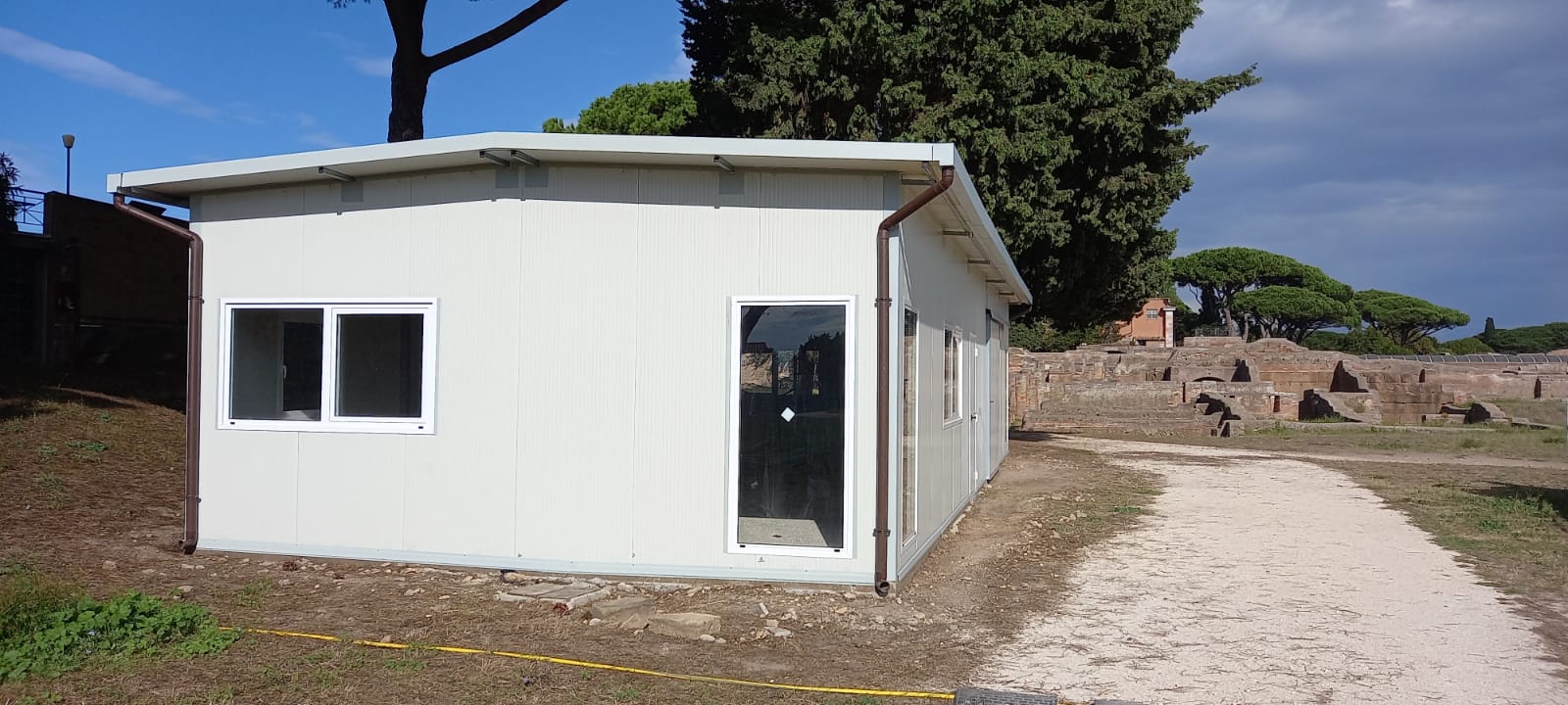 Vicino a un sentiero di ghiaia si trova un piccolo edificio rettangolare bianco con una finestra e una porta.