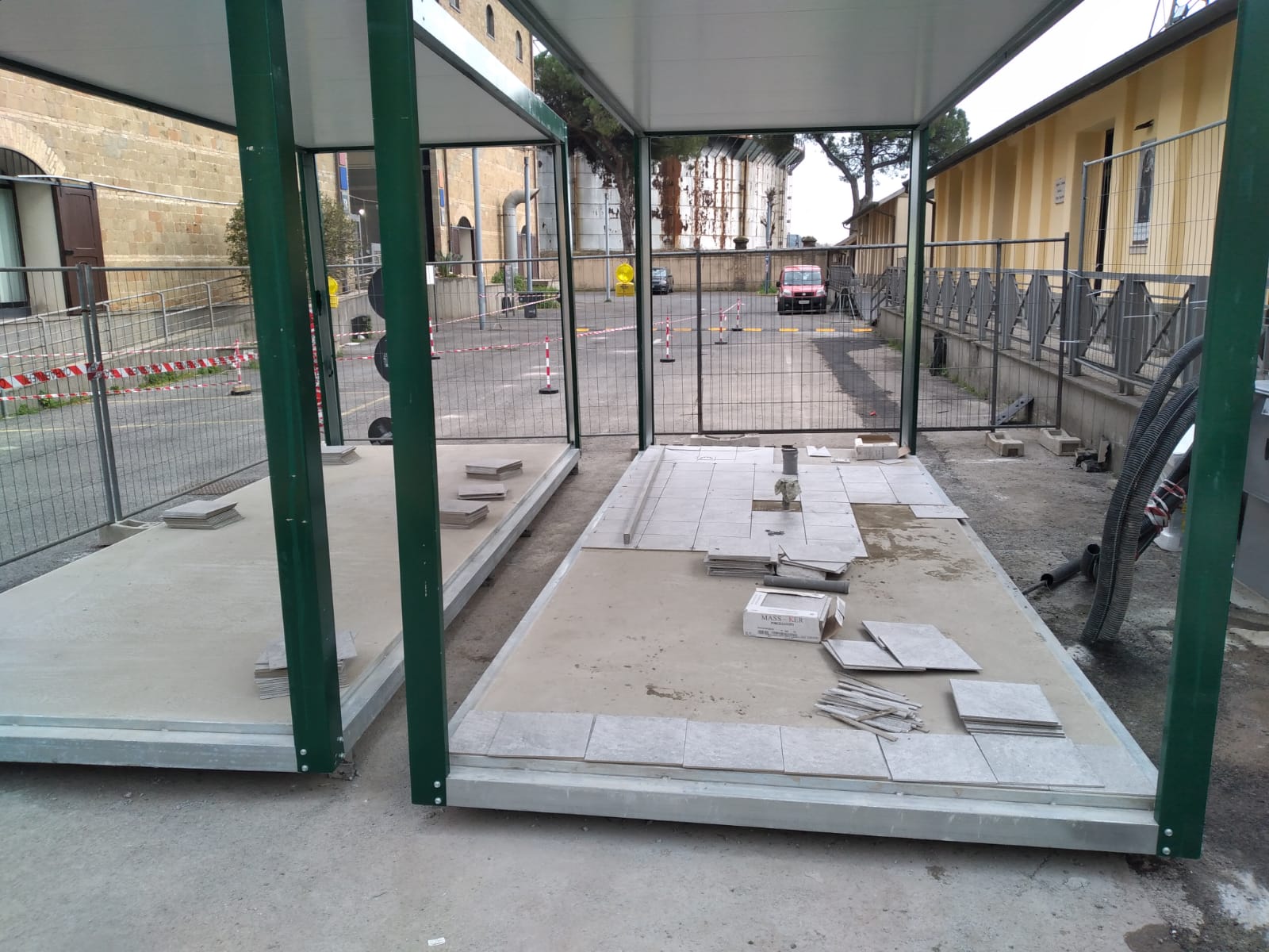Cantiere con due piattaforme coperte, piastrellatura incompleta e ingresso con cancello.