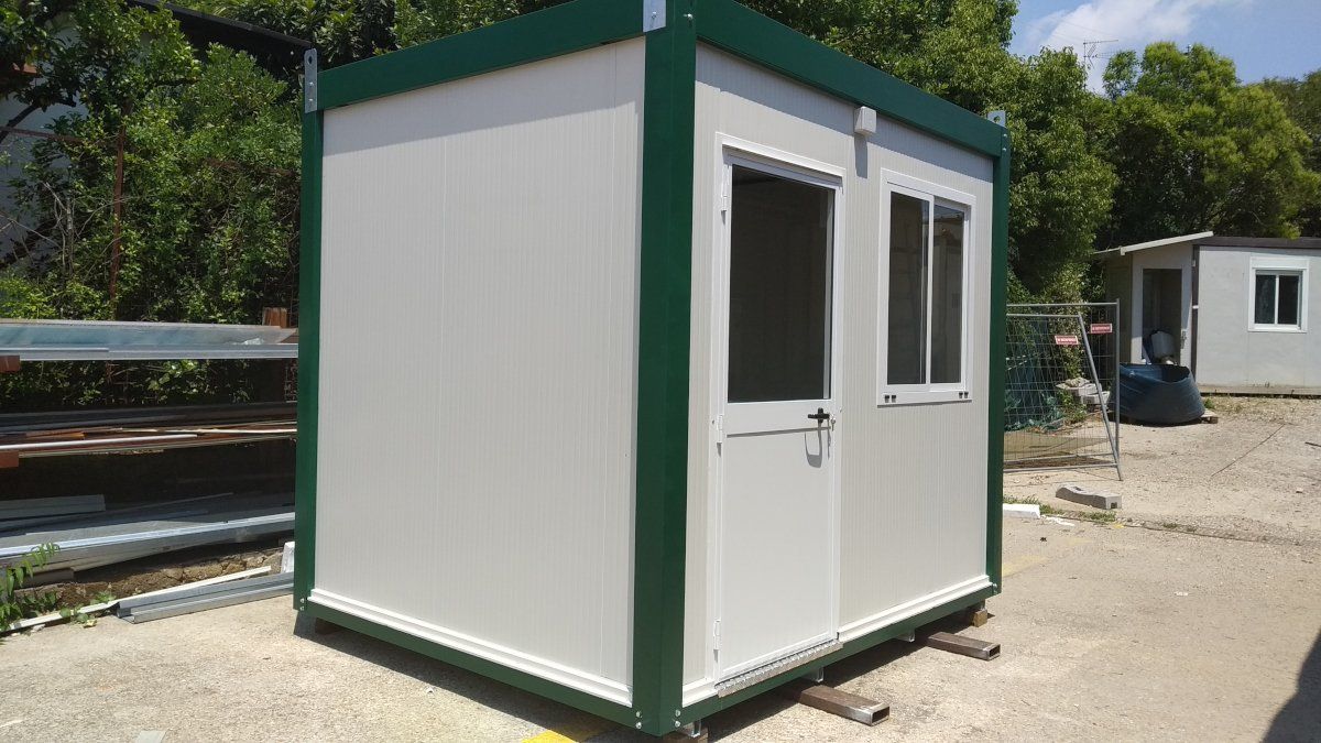 Edificio prefabbricato bianco e verde con porta e finestra all'esterno.