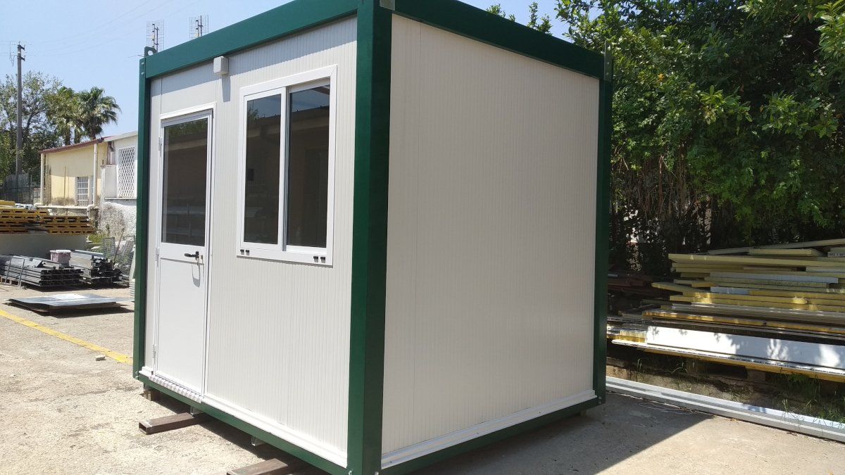 Edificio modulare bianco e verde con porta e finestre. Esterno, giornata di sole.
