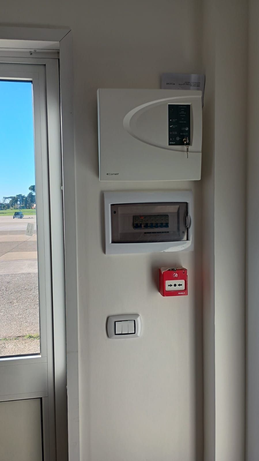 Parete bianca con sistema di allarme, quadro elettrico, allarme antincendio e interruttore della luce. 